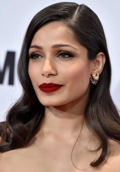 an image of a woman with long dark hair wearing red lipstick and gold earring