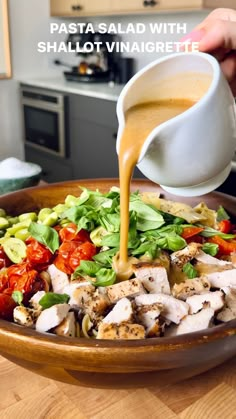 someone pouring dressing into a salad in a bowl with tomatoes, lettuce and chicken