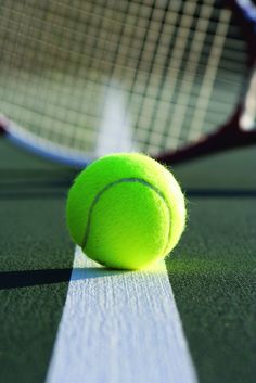 a tennis ball sitting on top of a court with a racquet in the background