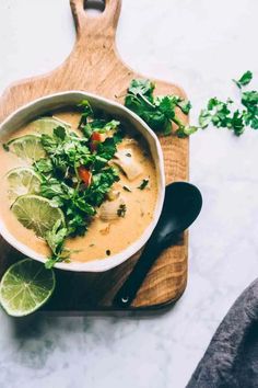 a bowl of soup with limes and cilantro on a wooden cutting board