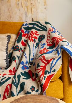 a yellow chair with a colorful blanket on it's back and pillows in the background