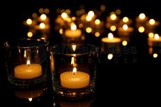 several lit candles are in glass cups on a black surface with reflections and blurry lights behind them