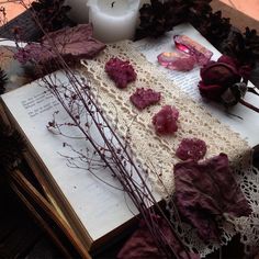 an open book sitting on top of a wooden table next to flowers and a candle