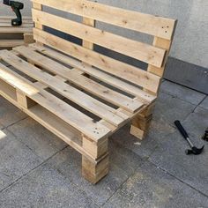 a wooden bench sitting on top of a sidewalk next to a cement wall with tools nearby