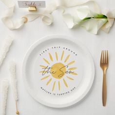 a white plate topped with a yellow sun on top of a table next to utensils