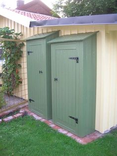 two green storage sheds sitting next to each other in the grass near a fence and building