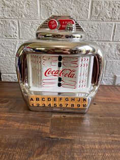 an old fashioned coca cola machine sitting on top of a wooden table