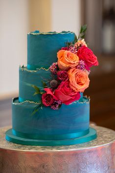 a three tiered cake with blue frosting and colorful flowers on it's side