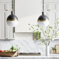 two pendant lights hanging over a kitchen counter with fruit and vegetables in the foreground