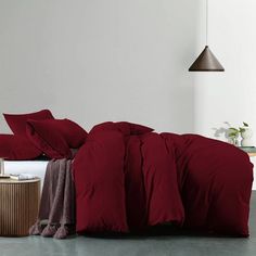 a bed with red sheets and pillows in a white room next to a wooden table