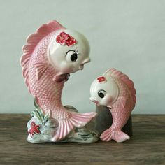 two fish figurines sitting next to each other on top of a wooden table