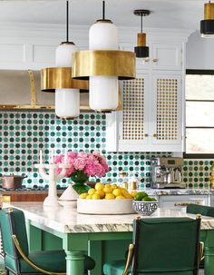 a kitchen with green chairs and white counter tops, gold chandelier over the island