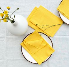 yellow napkins on plates with flowers in vase next to them and white ceramic pitcher