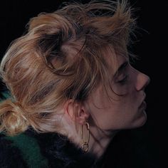 a woman with blonde hair wearing gold hoop earrings and black fur coat looking off to the side