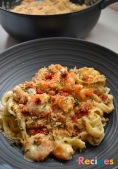 pasta with shrimp and tomato sauce in a black bowl next to a skillet on a white table