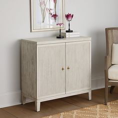 a white cabinet sitting next to a chair in front of a painting on the wall