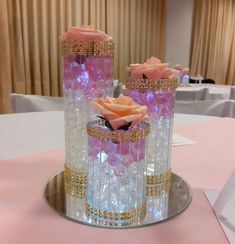 two vases with roses in them sitting on a pink and white table cloth covered table