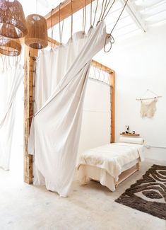 a bed with white sheets hanging from it's headboard in a room filled with furniture