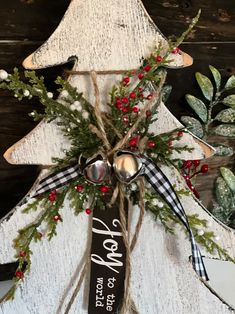 a white wooden christmas tree with red berries and greenery hanging from it's side