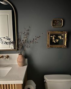 a white toilet sitting next to a sink in a bathroom under a framed painting on the wall