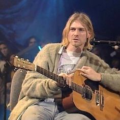 a man sitting in front of a microphone while holding a guitar