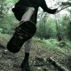 a woman in black dress and stockings carrying a suitcase through the woods with trees behind her