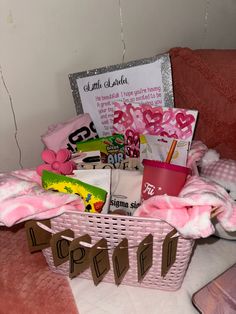 a pink basket filled with lots of stuff on top of a bed next to a sign