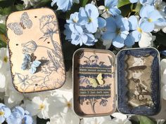 three tins with different designs on them and blue flowers in the background, one is empty