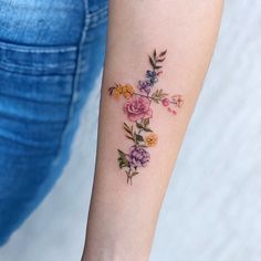 a woman's arm with flowers on it and a cross tattooed on the wrist