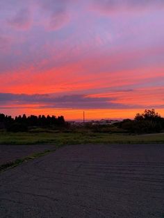 the sky is pink and purple as the sun sets in the distance behind some trees