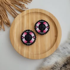 two pink and black beaded earrings on a wooden plate