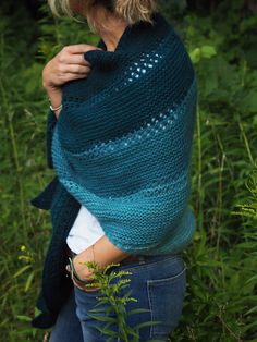 a woman wearing a blue knitted shawl standing in tall grass