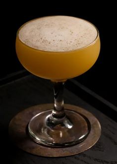 a glass filled with liquid sitting on top of a wooden table next to a black wall