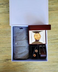 an open box containing a watch, tie, and other items on a wooden table