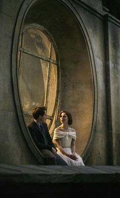 a man and woman sitting in front of an oval window looking into each other's eyes