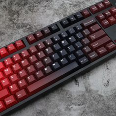 a red and black keyboard sitting on top of a stone floor next to a mouse