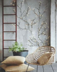 a chair and some pillows in front of a wall with lights on the branches behind it