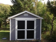 a gray shed sitting in the middle of a field next to some trees and bushes