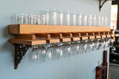 several wine glasses are lined up on a wooden shelf with metal brackets and glass holders