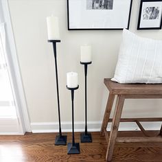 three candles are on the floor next to a bench and framed pictures in a living room