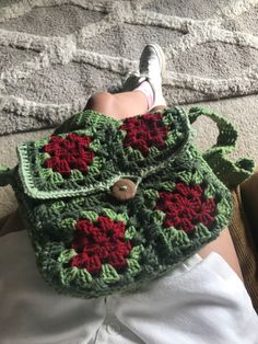 a crocheted purse with red and green flowers sitting on top of someone's lap