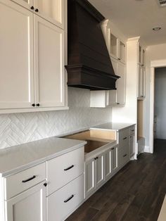 an empty kitchen with white cabinets and black hood over the stove top, in front of a wooden floor