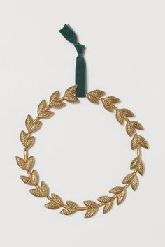 a gold bracelet with leaves is hanging on a green cord and has a blue ribbon around it