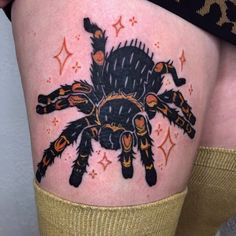 a woman's thigh with a black spider tattoo on it and gold stars around her legs