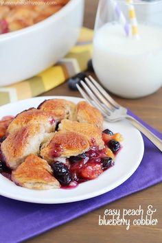 a white plate topped with blueberry cobbler next to a glass of milk and fork