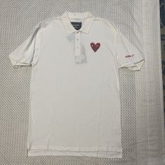 This Reason Clothing Polo Shirt Features An Embroidered Heart Design, Perfect For Any Occasion. The Shirt Is Made Of 100% Cotton And Has A Regular Fit, With Short Sleeves And A Collared Neckline. It Comes In Black And Is Available In Size L. The Shirt Is Machine Washable And Has Button Closure. It's Suitable For Various Activities Such As Tennis, Walking, School, Golf, Dance, Driving, And Fishing. The Shirt Is Part Of The Keith Haring Product Line And Is Perfect For Men Who Want To Make A Statem Casual Embroidered Collared Tops, Casual Cotton Shirt With Heart Print, Casual Polo T-shirt With Embroidered Logo, Casual Polo Collar Top With Embroidered Logo, Casual Collared T-shirt With Embroidered Logo, Embroidered Cotton Collared Tops, Casual Embroidered Cotton Polo Shirt, Casual Cotton Embroidered Polo Shirt, Embroidered Cotton Polo Shirt