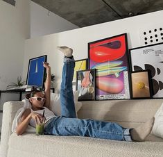 a man laying on top of a couch with his feet up in the air while holding a drink