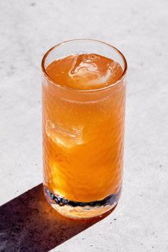 a glass filled with liquid sitting on top of a white counter next to a shadow