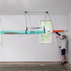 a man standing in front of a surfboard suspended from the ceiling with two paddles