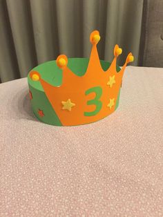 a green and orange crown sitting on top of a table next to a pink curtain